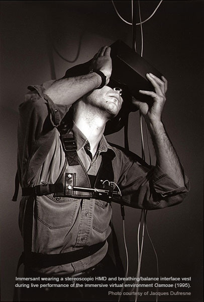 Immersant wearing a stereoscopic HMD and breathing/balance interface vest during live performance of the immersive virtual environment Osmose (1995). Photo courtesy of Jacques Dufresne.